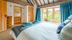 Un dormitorio con una cama grande, vigas de madera, un armario y una ventana con cortinas.