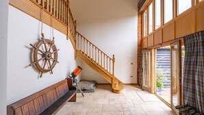 Una escalera con barandillas de madera que lleva a un segundo piso, un telescopio en el suelo y un ventanal con cortinas.