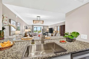 A kitchen with granite countertops, a stainless steel sink, and a dining area with a table and chairs.