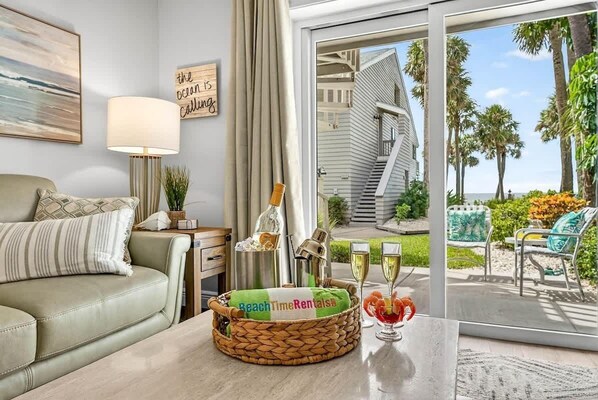 A living room with a sofa, a lamp, a basket with a towel, and a glass table with drinks.