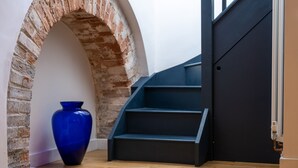 Una scala con finitura scura, un vaso azzurro e un arco in mattoni.