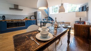 Una cucina moderna con mobili blu, un tavolo da pranzo in legno apparecchiato con piatti e ciotole bianche, e lampade a sospensione.