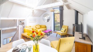 Un espace de vie lumineux et décloisonné, avec un canapé jaune, une table à manger et ses chaises, un meuble en bois et une grande fenêtre.