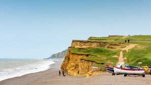 Une plage avec des bateaux, une falaise et un sentier.