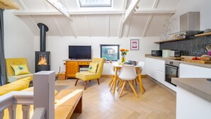 Un salon moderne avec une cheminée, des fauteuils jaunes, une table à manger et un coin cuisine avec un poêle noir.