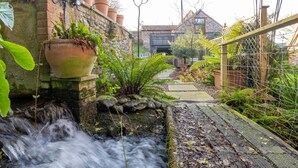 Un jardin avec un petit ruisseau, un mur de briques et des plantes en pot.
