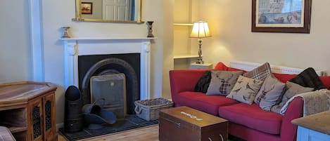 A cozy living room with a fireplace, a red sofa, a wooden cabinet, and a framed picture on the wall.