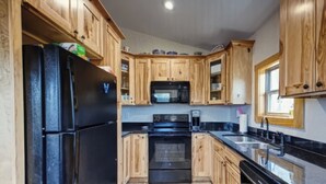 A kitchen with wooden cabinets, a black refrigerator, a microwave, and a stove. - The Lake Cottage on the Peninsula.  (Dandridge)