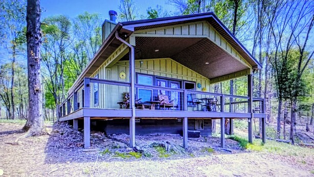 A cabin with a covered deck and multiple windows, surrounded by trees. - The Lake Cottage on the Peninsula.  (Dandridge)