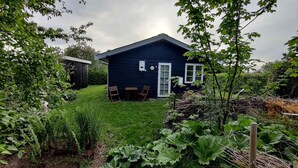 A dark blue house with a small garden, two wooden chairs, and a table outside. - 5 Star Holiday Home in Kirke Hyllinge (Kirke Hyllinge)