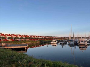 A marina with boats docked, a wooden pier, and red buildings with white trim in the background. - 4 Star Holiday Home in Ebeltoft (Ebeltoft)