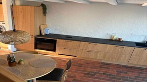 A modern kitchen with a brick floor, wooden cabinets, a round dining table, and a hanging light fixture. - 4 Star Holiday Home in Ebeltoft (Ebeltoft)