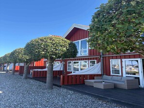 A row of red wooden cabins with white windows, a gravel path, and a tree in the foreground. - 4 Star Holiday Home in Ebeltoft (Ebeltoft)
