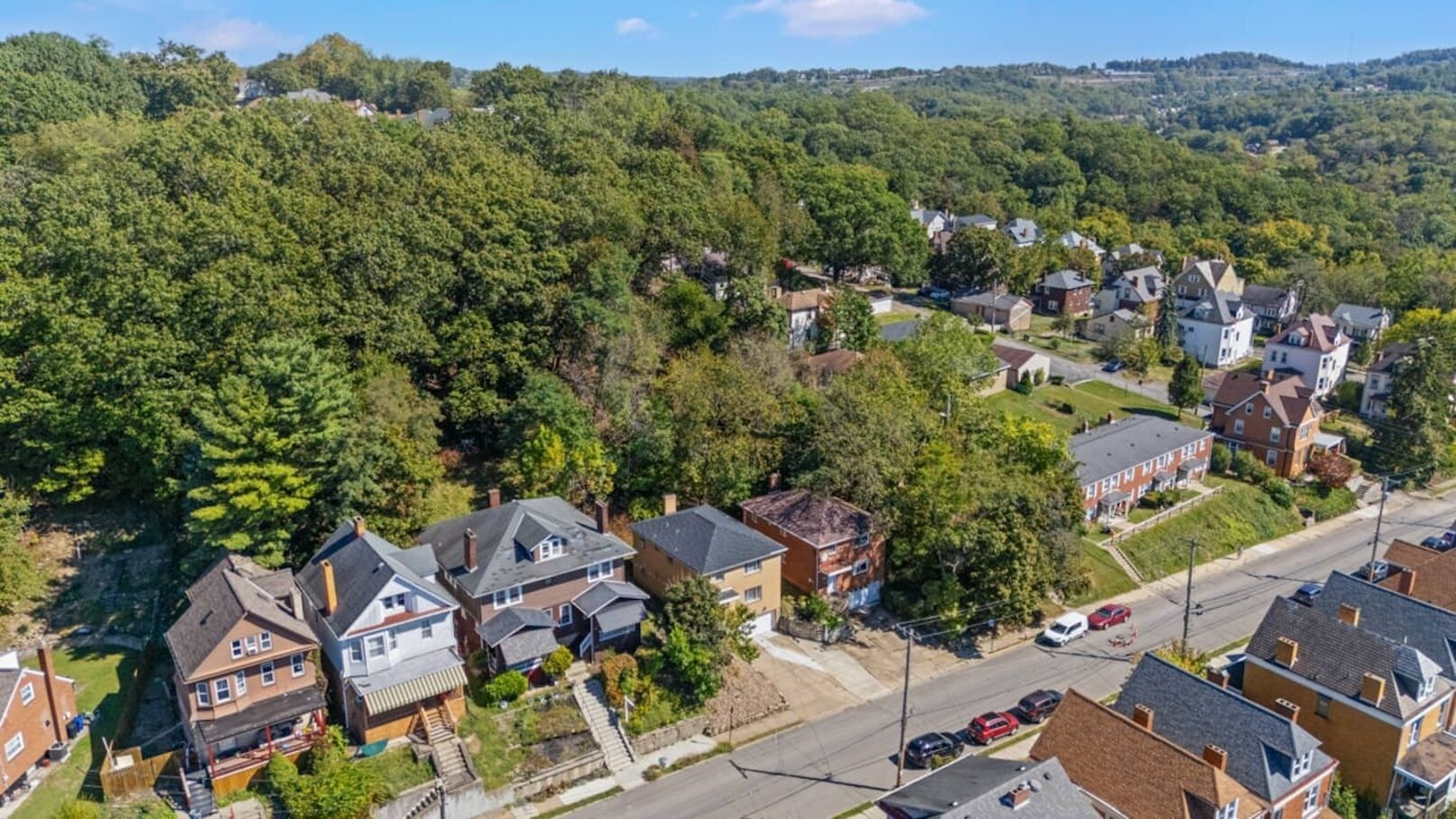 An aerial view of a residential area with houses, streets, and a hilly landscape in the background.