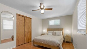 Un dormitorio con cama de madera, ventilador de techo, mesita de noche con espejo y armario.