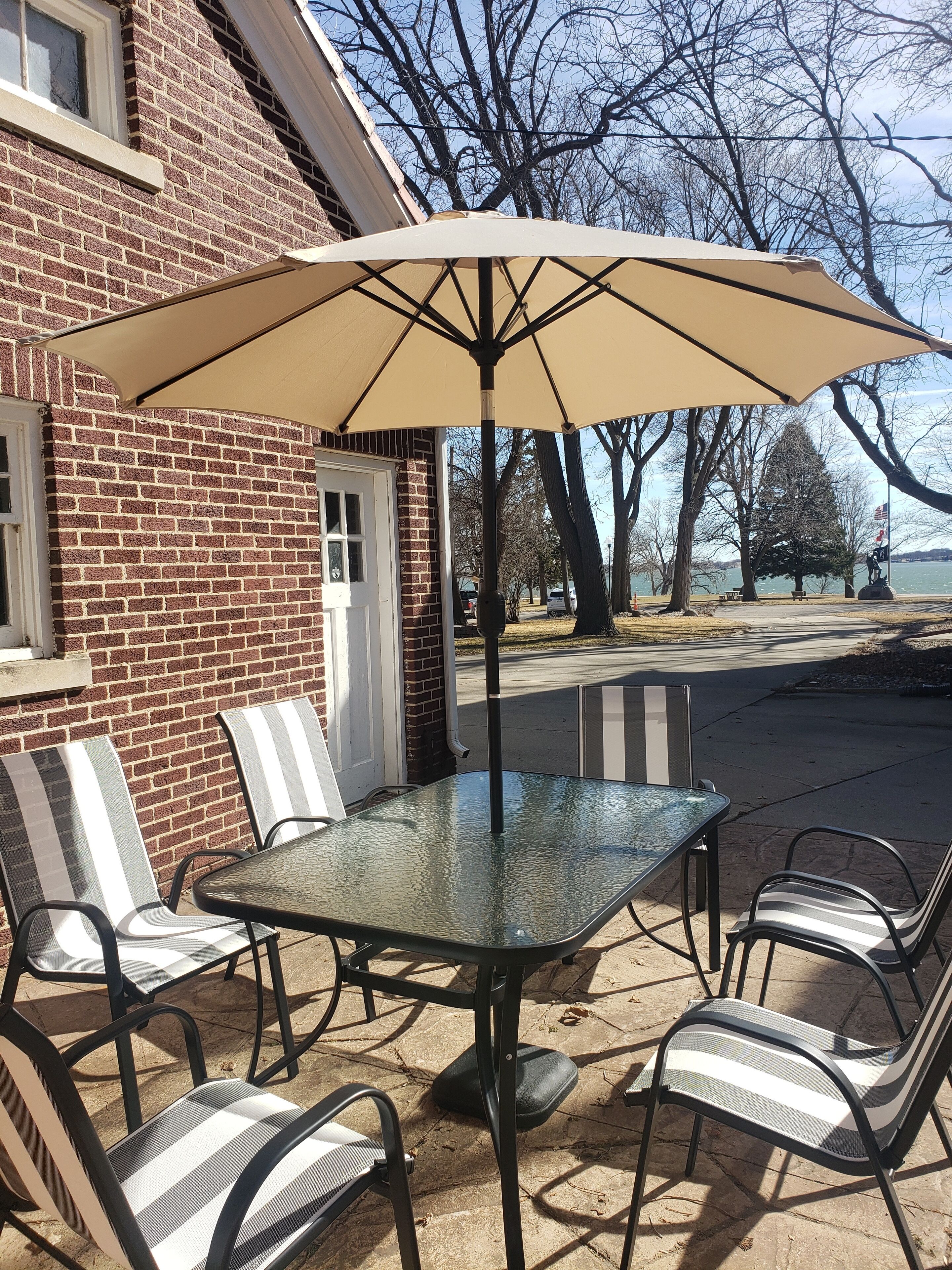 En terrasse med et glasbord og stribede stole, en parasol samt en murbygning i baggrunden.