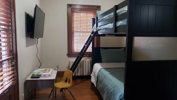 Ein Schlafzimmer mit Etagenbett, Schreibtisch mit Stuhl, Wandfernseher und Fenster mit Jalousien.