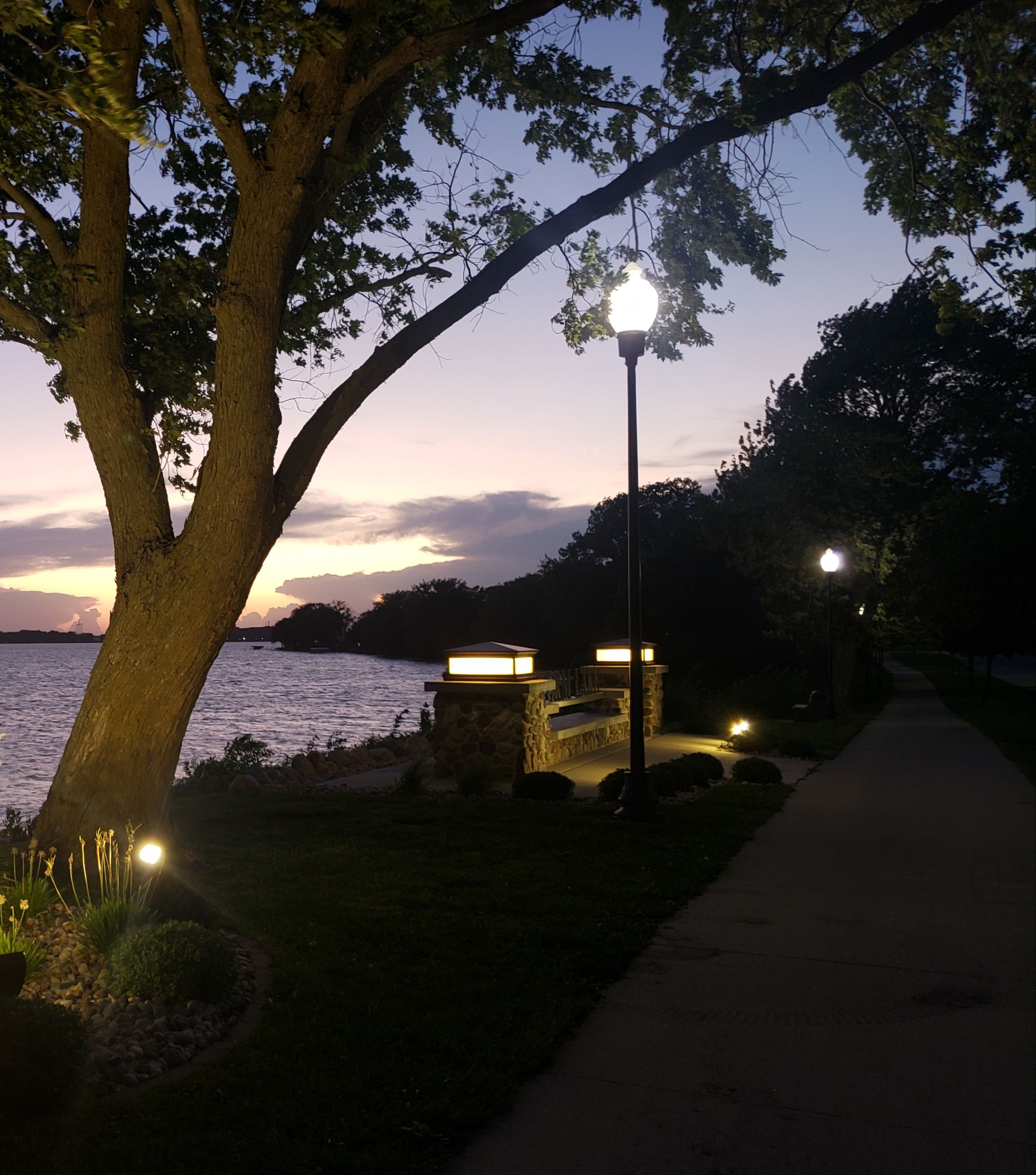 A pathway beside a body of water with a stone structure and a lamp post.