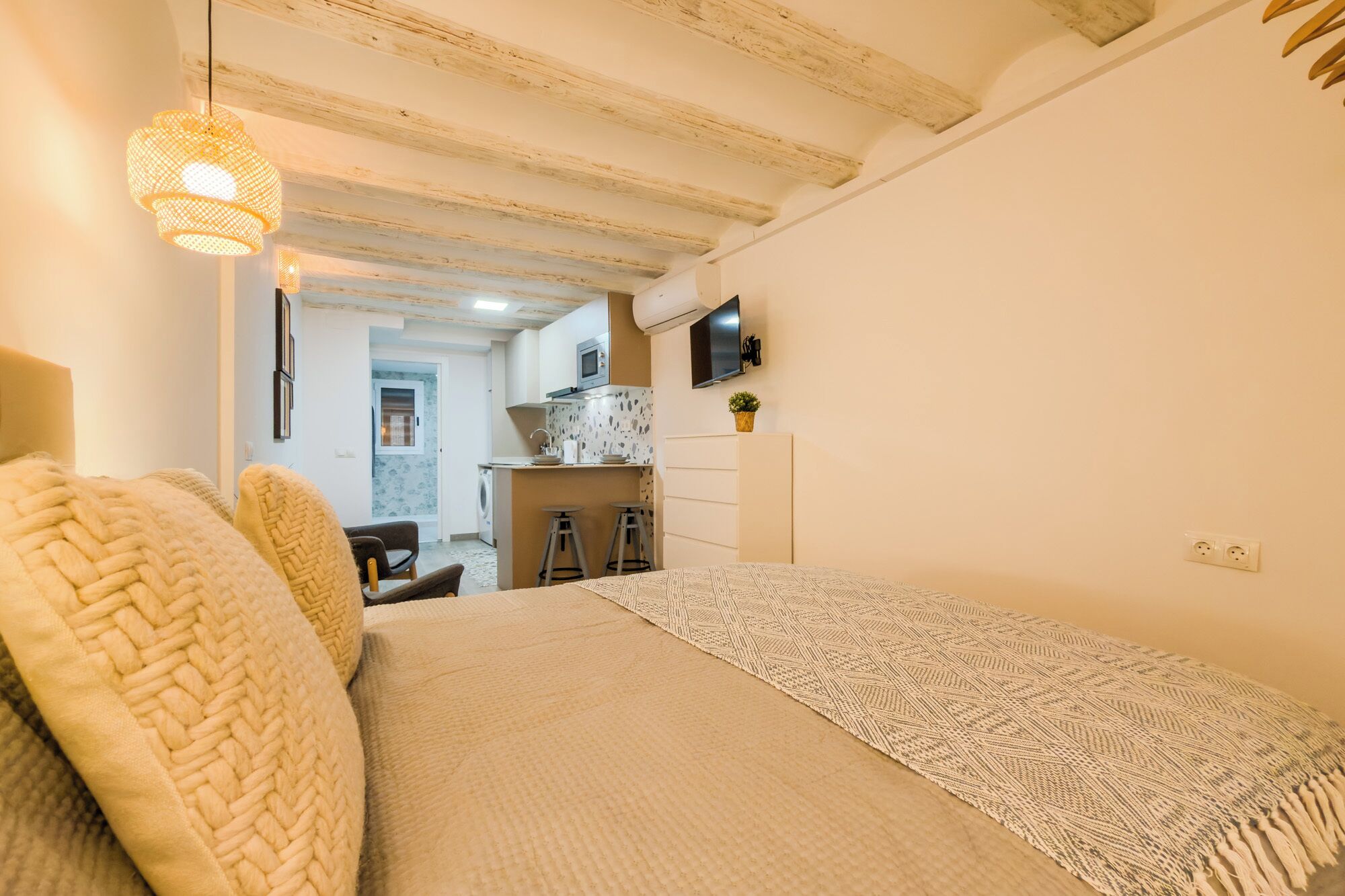 A bedroom with a bed, a desk, a chair, and a television on the wall.