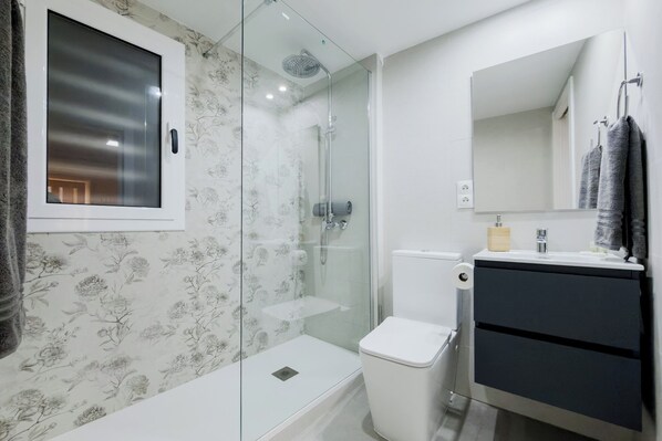 A modern bathroom with a glass shower enclosure, a toilet, and a vanity with a mirror.