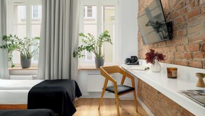 Une pièce avec un mur en briques, un téléviseur à écran plat, deux plantes en pot, une chaise en bois et un comptoir blanc avec une machine à café.