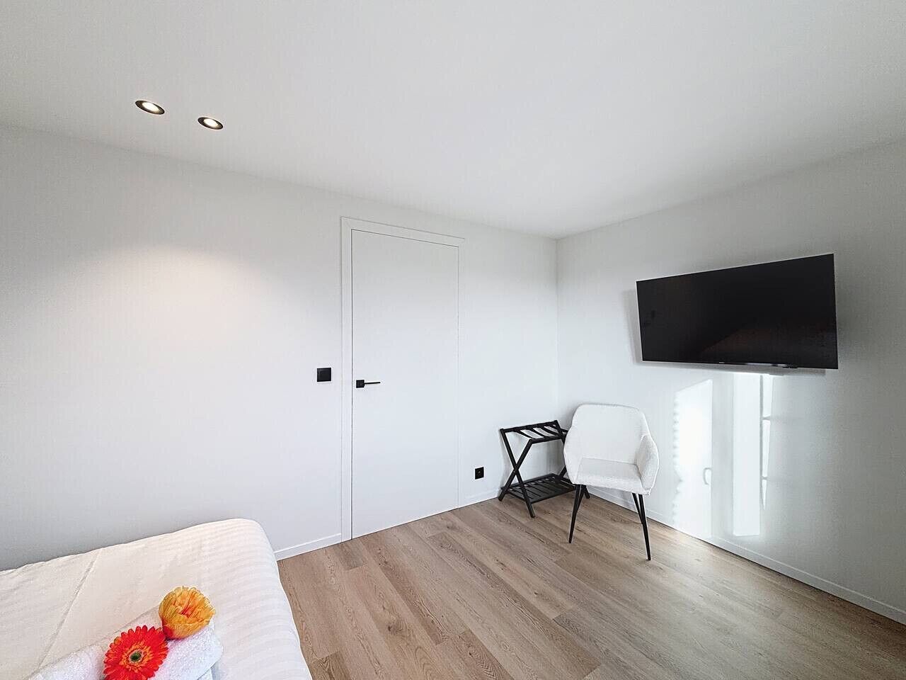 A modern hotel room with a bed, a desk, and a TV mounted on the wall.