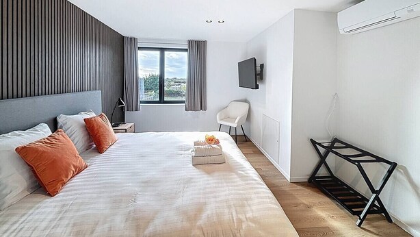 Habitación de hotel moderna con una cama grande, un televisor montado en la pared y vistas al exterior por la ventana.