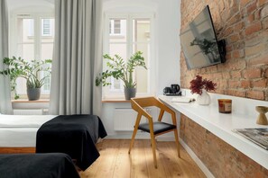 A room with a brick wall, a flat-screen TV, two potted plants, a wooden chair, and a white counter with a coffee machine.
