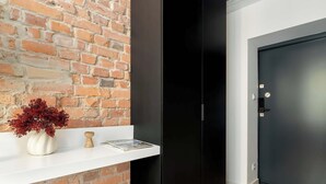 A room with a brick wall, a white shelf with a vase and a book, a black wardrobe, and a dark door.