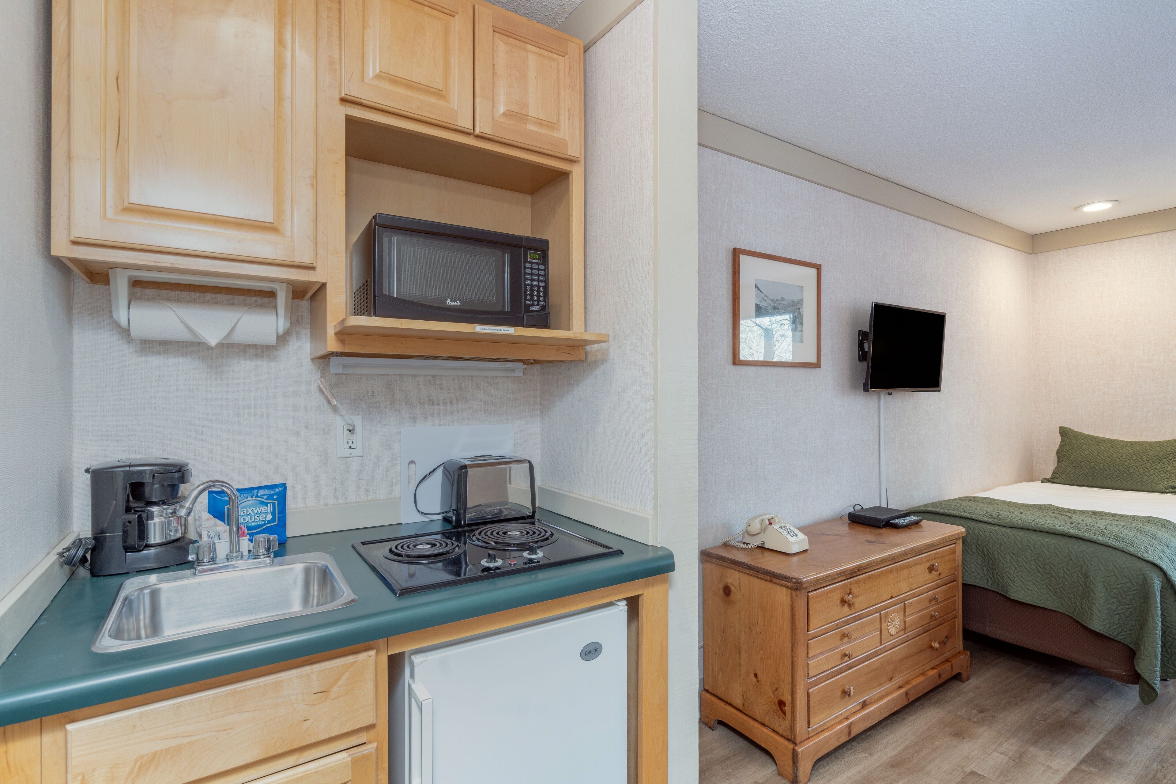 Een compacte kitchenette met een magnetron, koffiezetapparaat en kleine koelkast.