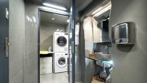 Un baño moderno con puerta de cristal, lavadora, lavabo con repisa de vidrio y barra para toallas.