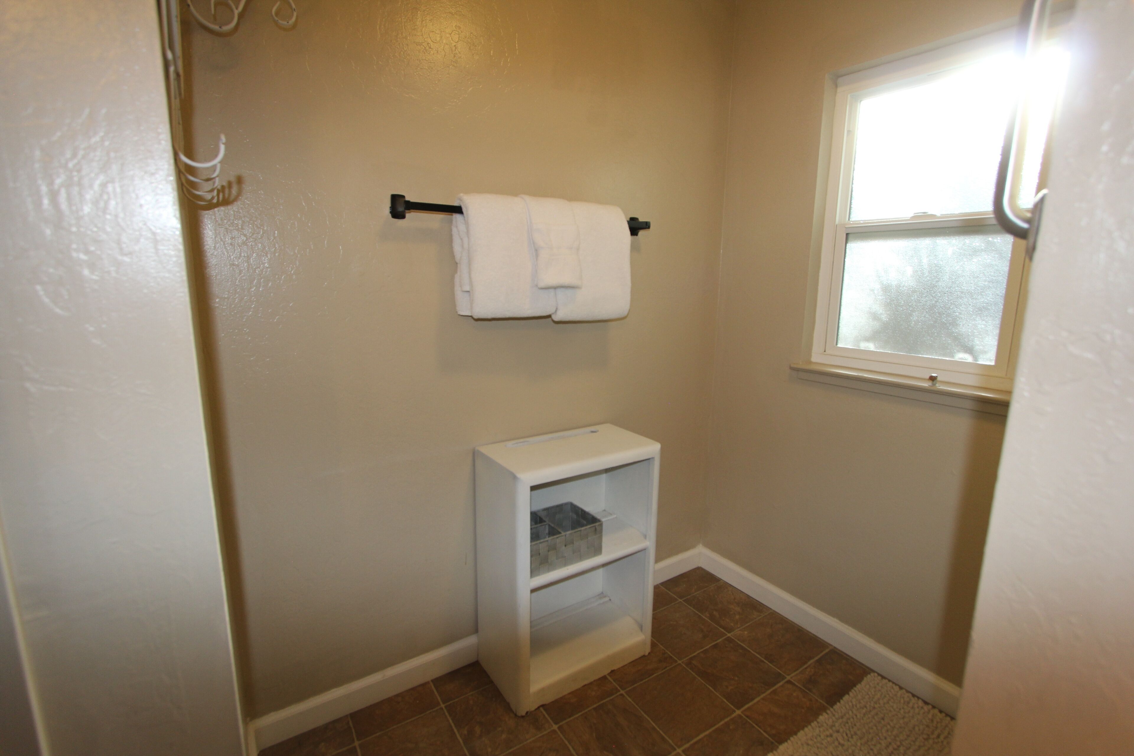 A small bathroom with a toilet, a shelf, and a window.