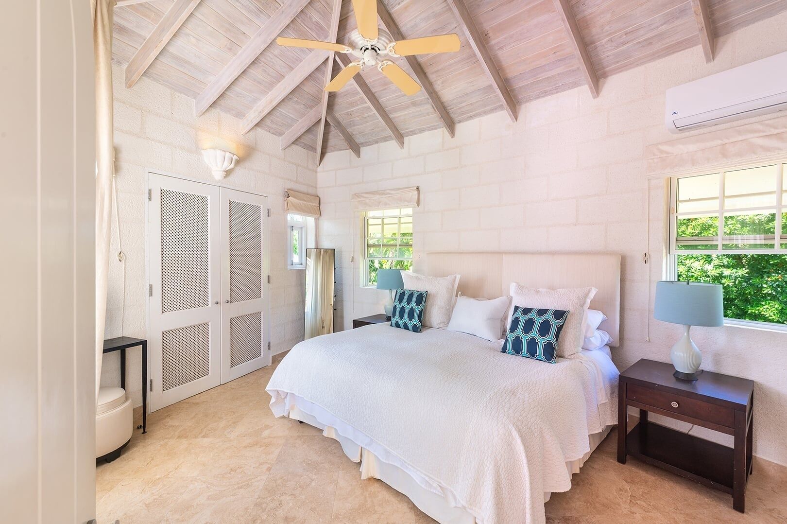 A bedroom with a bed, nightstands, a ceiling fan, a window, and a door with a mesh screen.