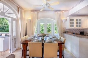 A dining room with a table set for four, a ceiling fan, and a view of greenery outside.