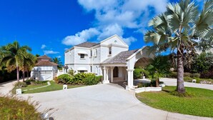A two-story house with a covered porch, a driveway, and surrounding palm trees. - Sugar Hill - Half Century House 6 Bedroom Villa (Holetown)