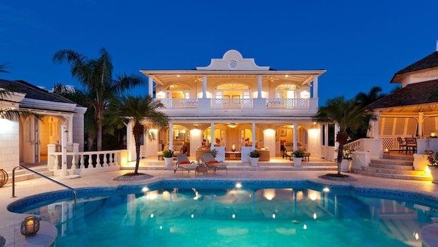 A large, two-story house with a swimming pool in front, surrounded by palm trees and well-lit outdoor areas. - Sugar Hill - Half Century House 6 Bedroom Villa (Holetown)