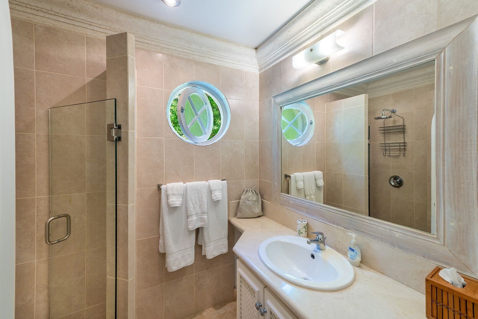 A bathroom with a glass shower enclosure, a sink with a mirror, and towels on a rack.