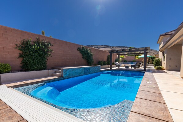 Une piscine avec un bord carrelé, une pergola et un mur en briques.