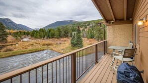 Un balcon avec vue sur une rivière et des montagnes, une table et des chaises, ainsi qu’un espace abrité avec un luminaire.