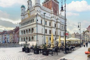 A historic building with ornate architecture, outdoor seating with umbrellas, and a cobblestone plaza.