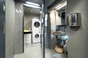 Ein modernes Badezimmer mit Glasdusche, Waschmaschine, Waschbecken mit Glastrennwand und Handtuchhalter.