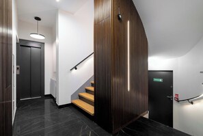 Ein modernes Interieur mit Treppe, einer Holzwand und einer schwarzen Tür mit Notausgangsschild.