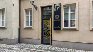 Rakennuksessa on beigenvärinen julkisivu, mustat ovet, joissa on geometrinen kuvio, ja kyltti, jossa lukee: ”Schoeps Residence Kramarska”.