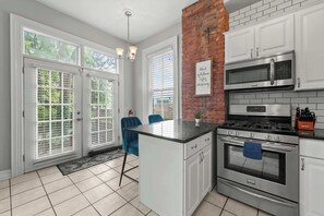 Een keuken met witte kastjes, een accentmuur van baksteen, een gasfornuis, een magnetron en een groot eiland met een spoelbak.