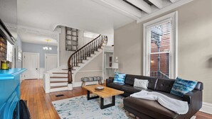 A living room with a staircase, a brown leather sofa, a wooden coffee table, and a blue patterned rug. - High Street Hideaway - For 8 (Columbus)