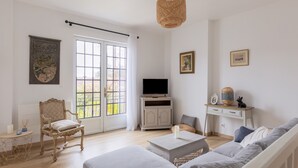 A living room with a sofa, a television, a wicker hanging light fixture, and a window with curtains. - 5 Minutes from Amboise in the Heart of the Châteaux (Limeray)