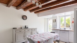 A kitchen with a dining table, white cabinets, a clock, and a window with a view of greenery. - 5 Minutes from Amboise in the Heart of the Châteaux (Limeray)
