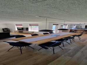A spacious conference room with a long wooden table, black chairs, and a television on a stand.