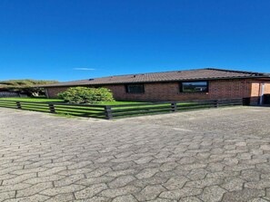 A brick building with a tiled roof, a paved driveway, and a wooden fence.