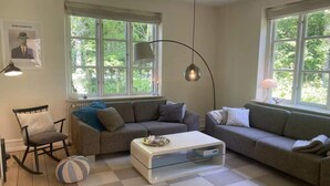 A living room with two sofas, a coffee table, a rocking chair, and large windows with a view of greenery. - 5 Star Holiday Home in Morkov (Morkov)